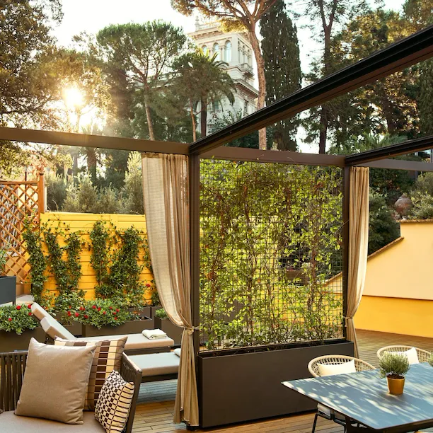 Sunny terrace with plants, couch, table for al fresco dining at Aurora Terrace Suite at Hotel Eden, Rome