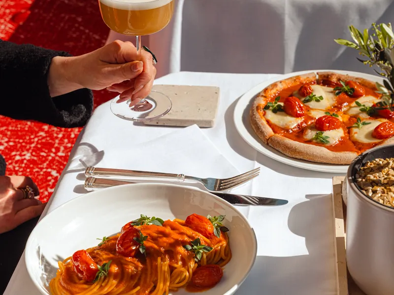 Pasta and pizza on a white table, a hand hold a cocktail.