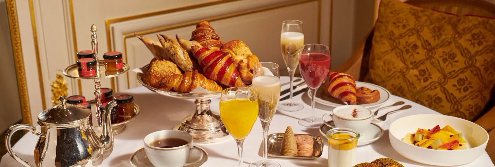 Images du brunch au Jean Imbert au Plaza Athénée. On peut voir en gros plan un petit pain, des salades, des oeufs et des pâtisseries disposés sur la table ainsi que des jus de fruits et du champagne.