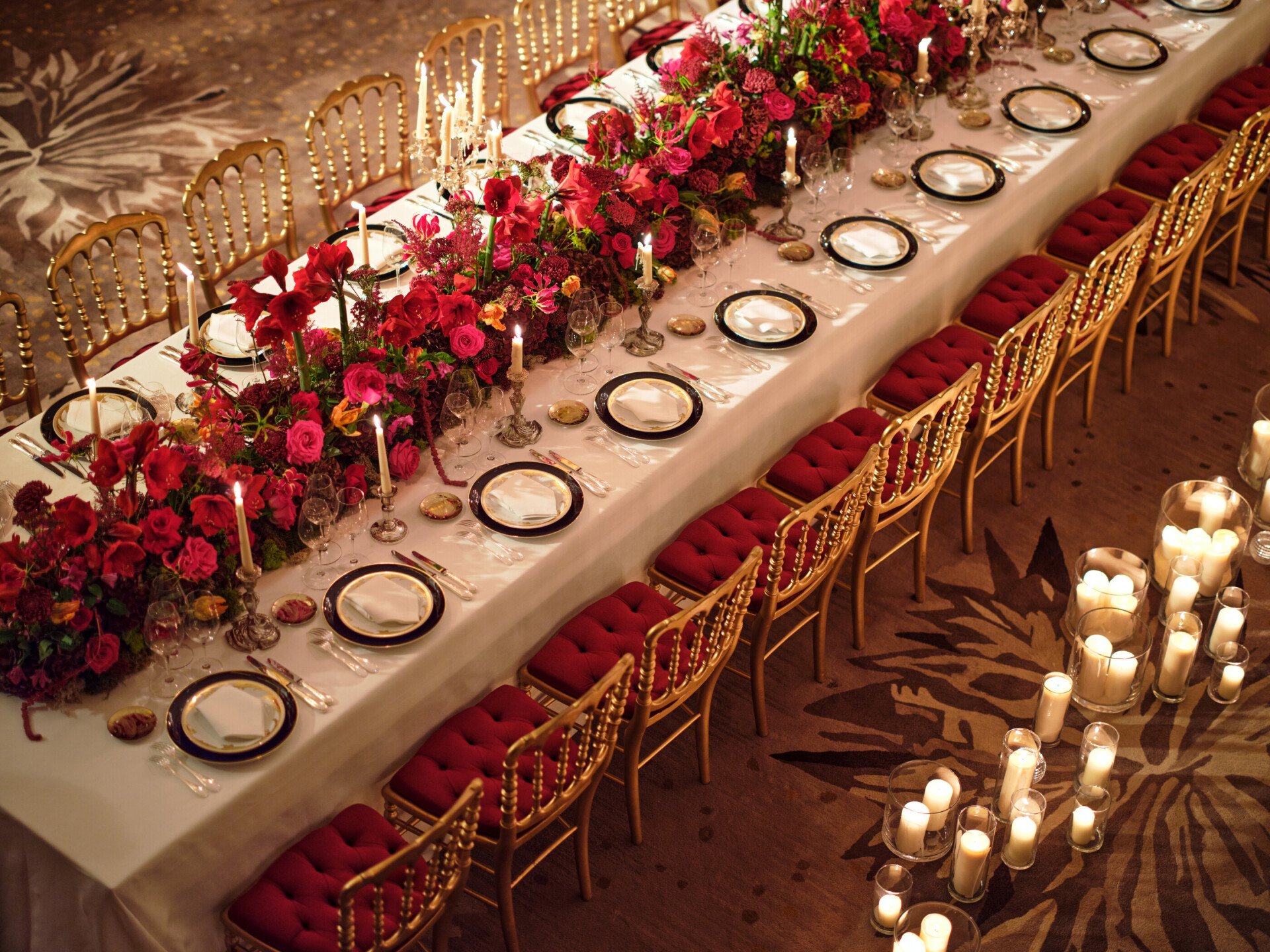 Dinner set up with a long table and red flowers captured in Le Salon Haute Couture, at Hôtel Plaza Athénée, Paris - Dorchester Collection.