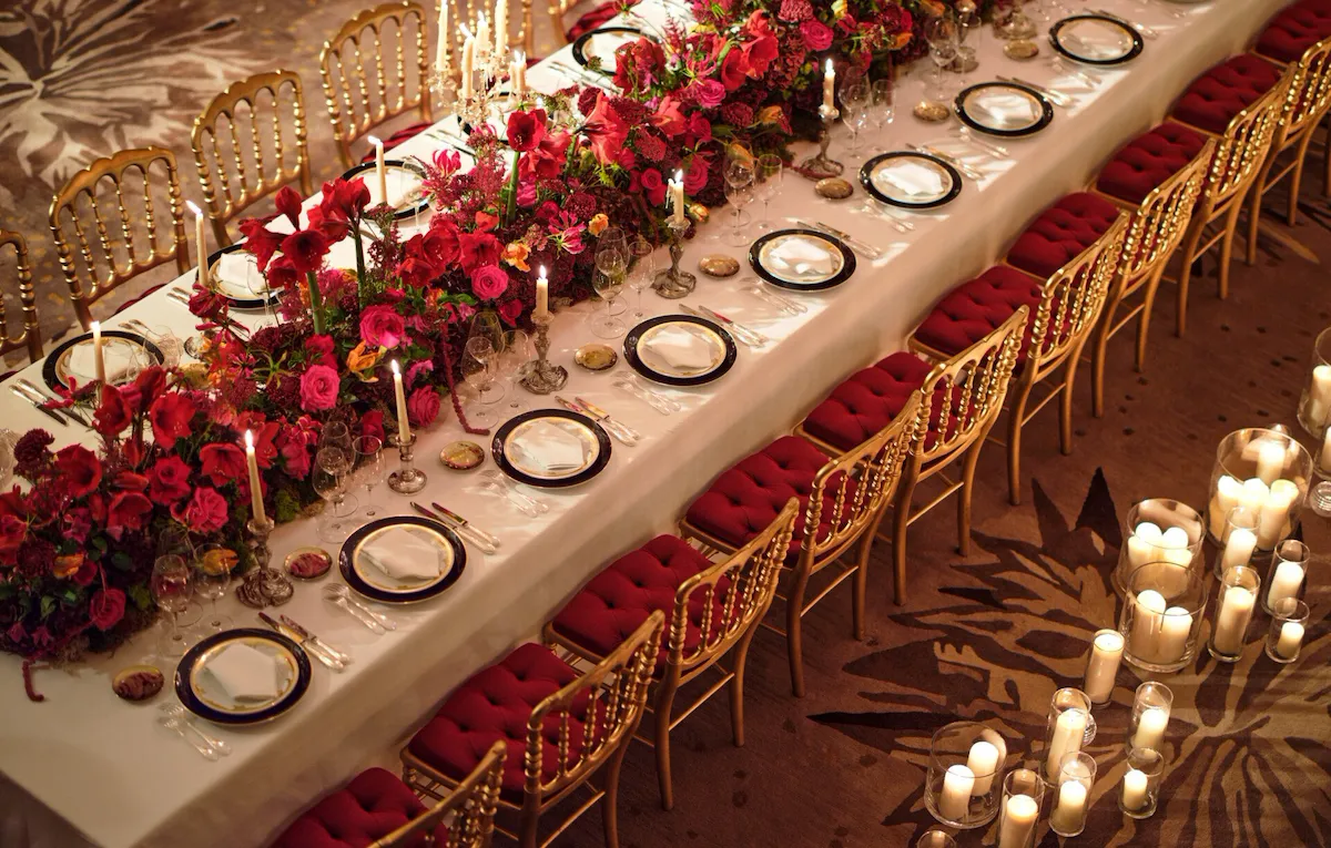 Dinner set up with a long table and red flowers captured in Le Salon Haute Couture, at Hôtel Plaza Athénée, Paris - Dorchester Collection.
