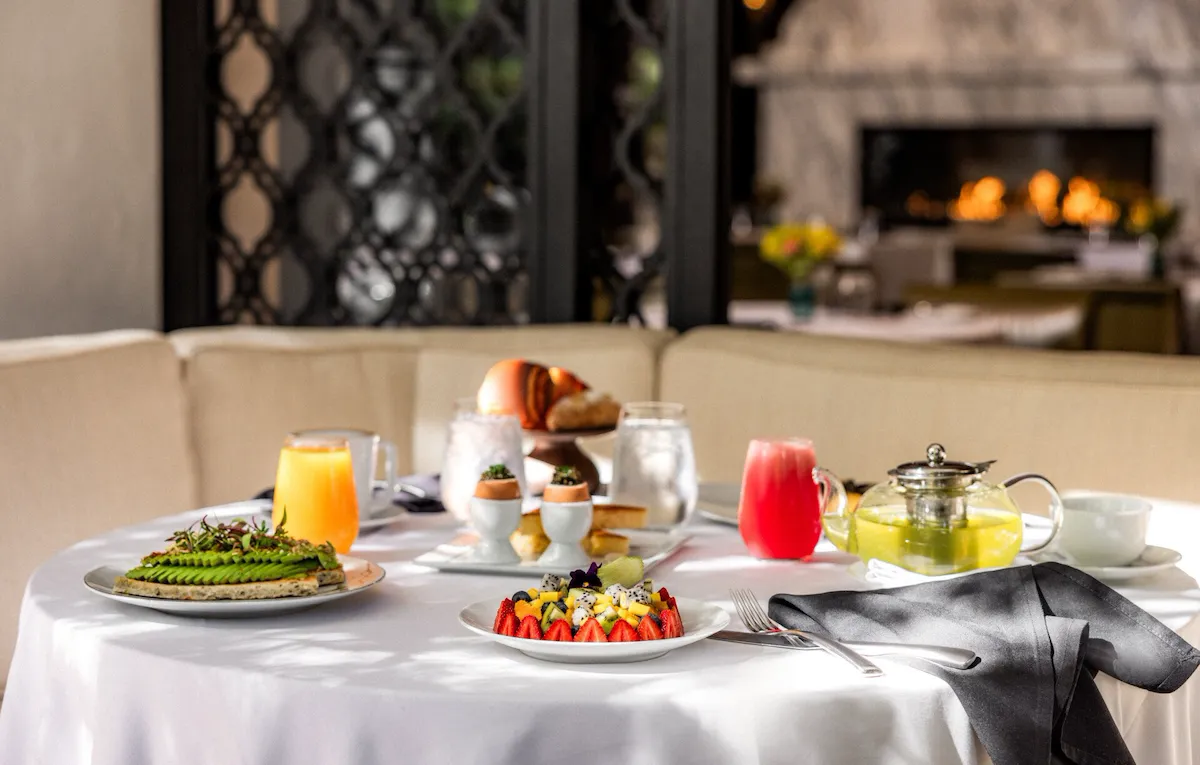 Breakfast at The Restaurant table spread featuring fruit platter, avocado toast, and juices