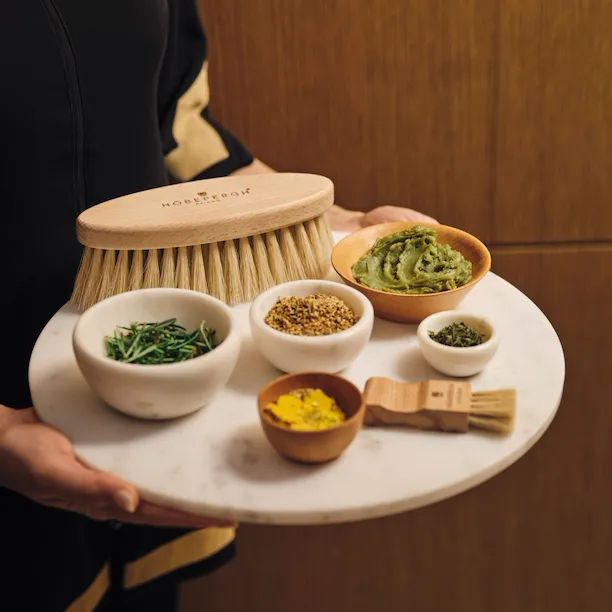 Spa therapist holding tray with brushes, small bowls with alpine herbs