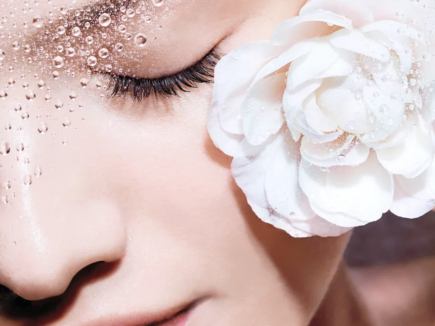 Photo of a nude face with the eyes closed and a white rose.