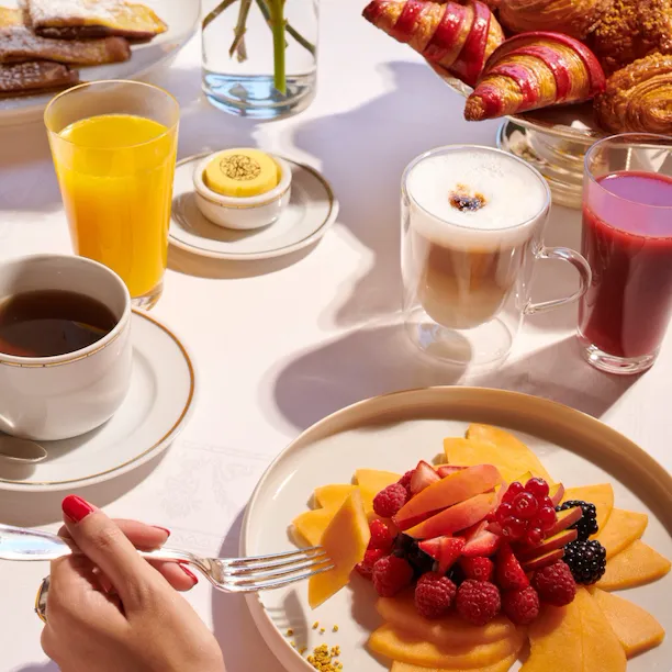 Images du brunch au Jean Imbert au Plaza Athénée. On peut voir une main qui cueille des fruits dans une assiette de salade de fruits.