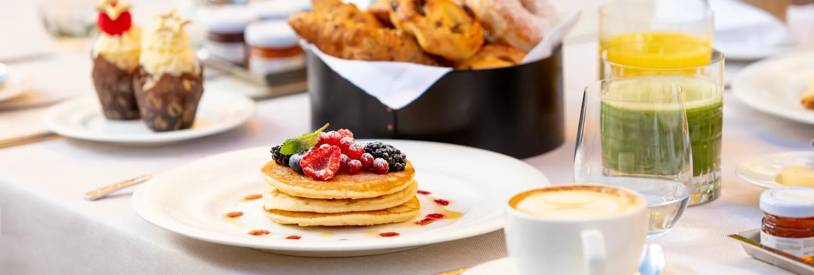 Tavolo de Il Giardino Ristorante apparecchiato per la colazione con tazza di cappuccino, piatto di pancake, cupcakes, selezione di cornetti