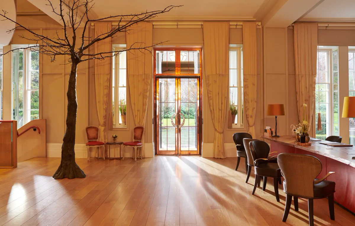 Entrance lobby doors and reception desk with sun streaming in at Coworth Park, Ascot