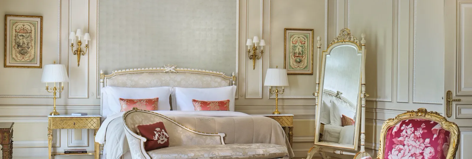Chambre élégante à la décoration vintage. Elle dispose d'un lit luxueux, d'un miroir orné d'un cadre doré, de chaises fleuries et d'un éclairage tamisé, évoquant une atmosphère classique et opulente.