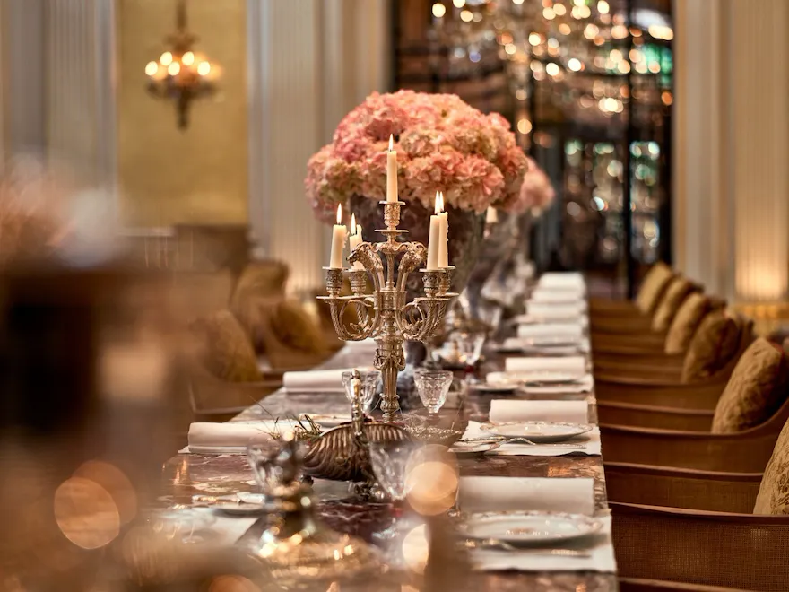 Jean Imbert au Plaza Athénée's central marble table, drawned up with pink flowers and candleholders. At Hotel Plaza Athénée, Paris