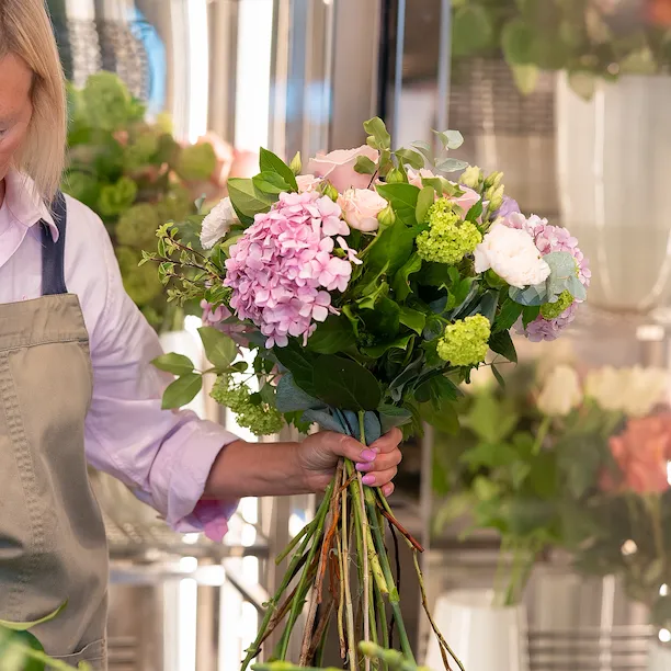 Florist assembling a pink floral bouquet with roses and hydrangeas at Cake & Flowers boutique
