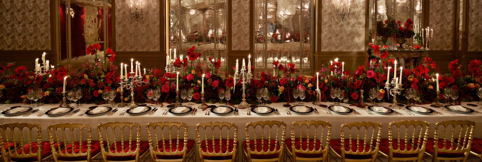 Dinner set up with a long table and red flowers captured in Le Salon Haute Couture, at Hôtel Plaza Athénée, Paris - Dorchester Collection.
