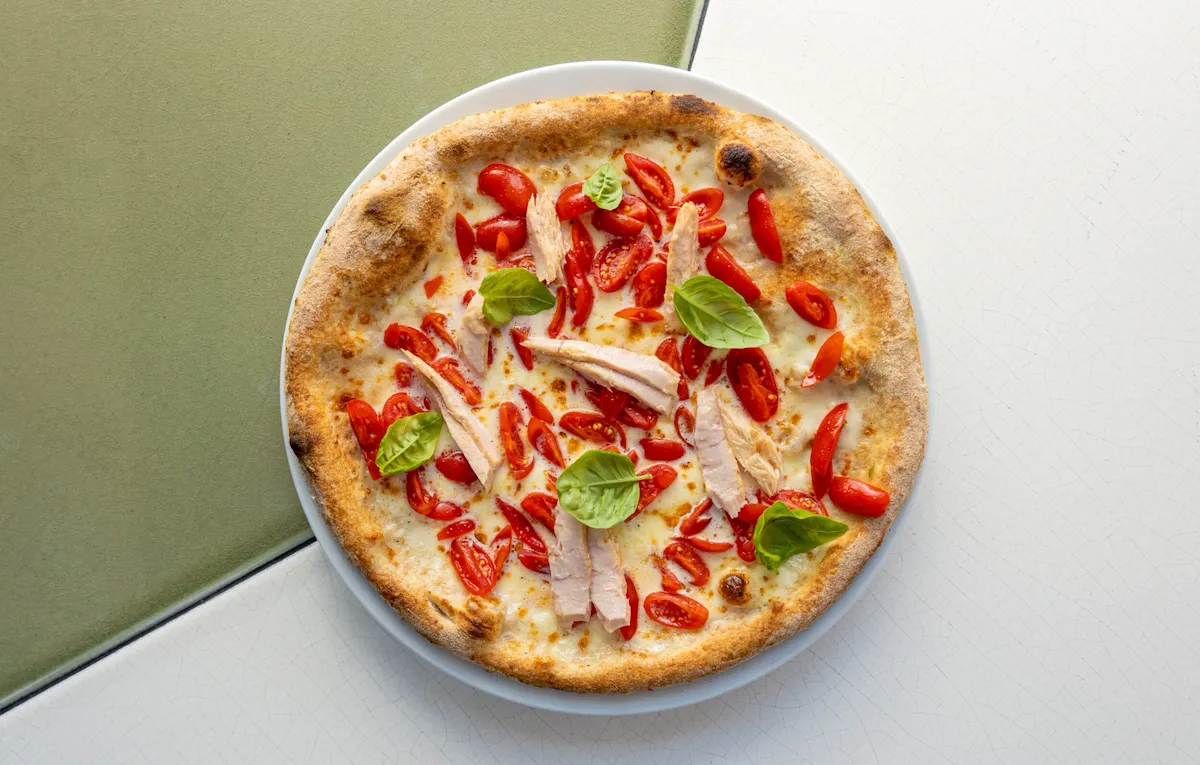 Pizza con pomodorini, mozzarella, tonno e basilico su di un tavolo de Il Giardino Ristorante a Hotel Eden Roma