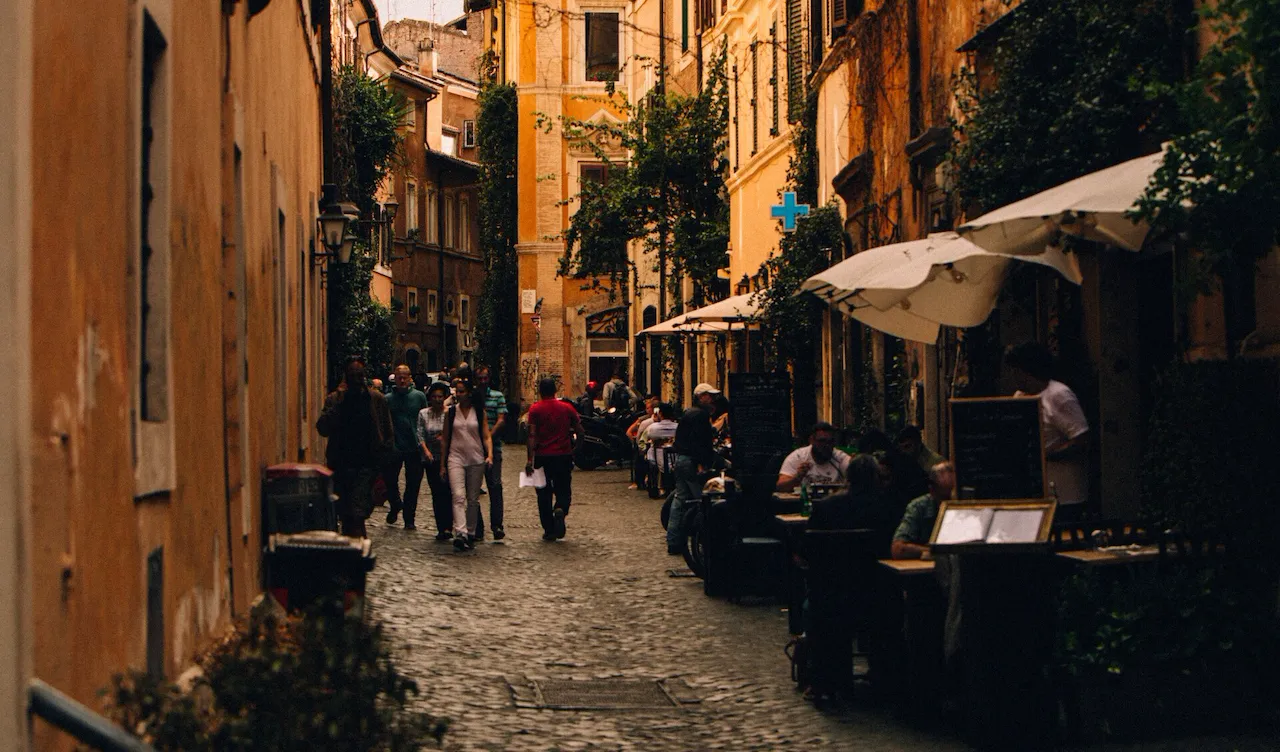 Un vicolo di Trastevere con persone che camminano davanti il dehors di un ristorante