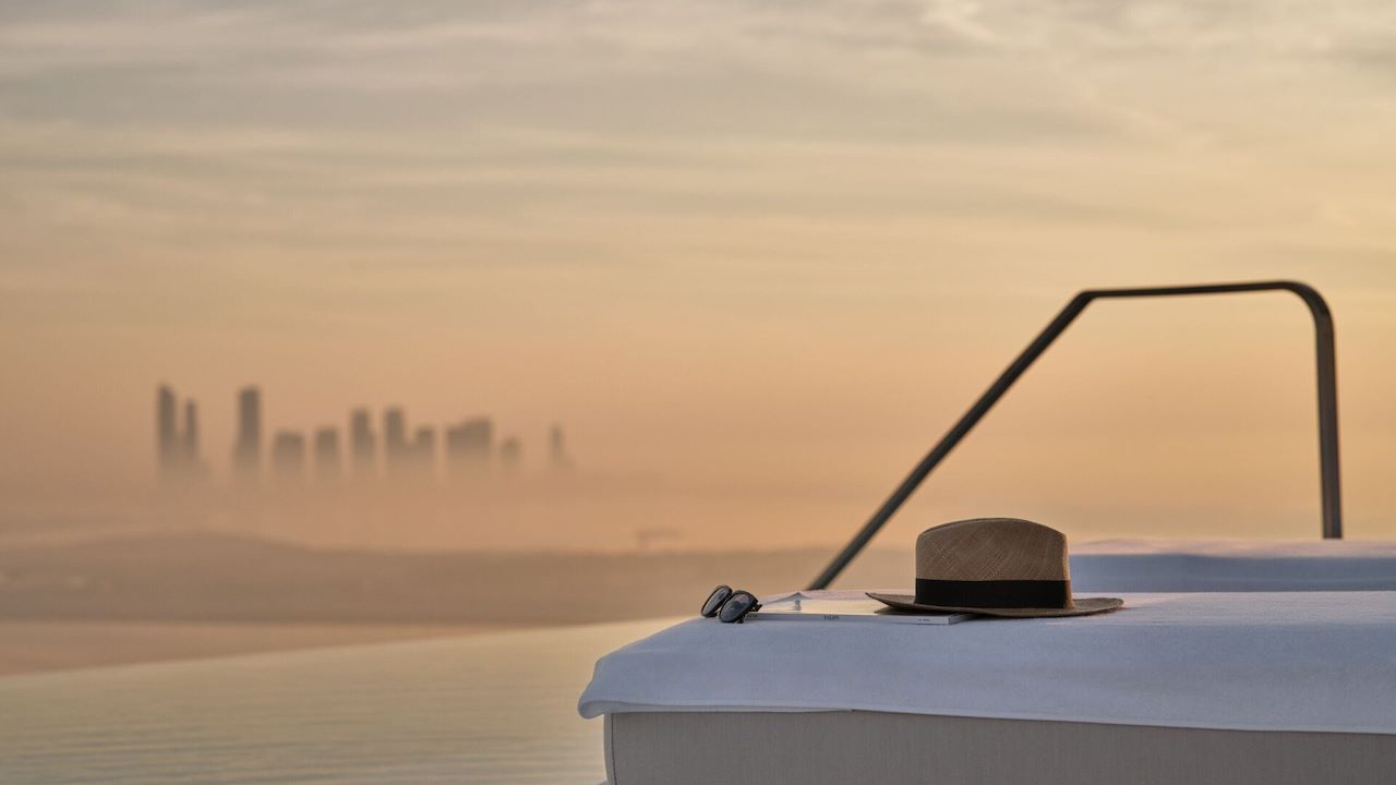 Detail of a hat on a sunlounger by The Lana's rooftop infinity pool at sunrise with view of Dubai