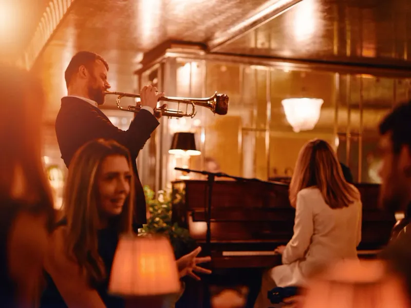 Two people playing trumpet and piano in the Vesper Bar in warm, evening light