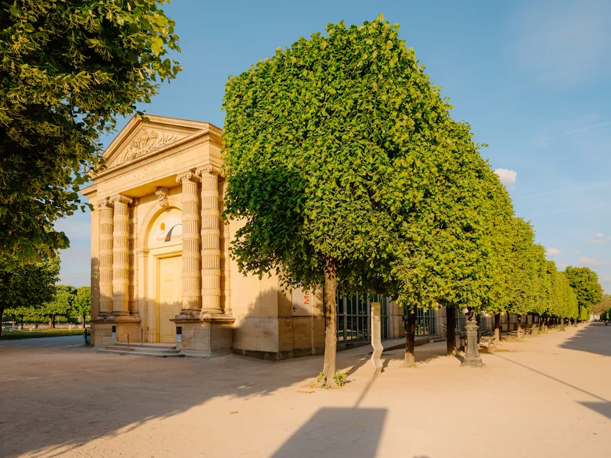 Entrance of the Musée de l'Orangerie with an alley of trees and a sunny blue sky, at Musée de l'Orangerie, Paris.