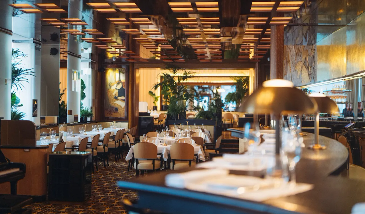 Overview of Le Relais Plaza's dining room lower deck, with the bar at the forefront,at Hotel Plaza Athénée, Paris
