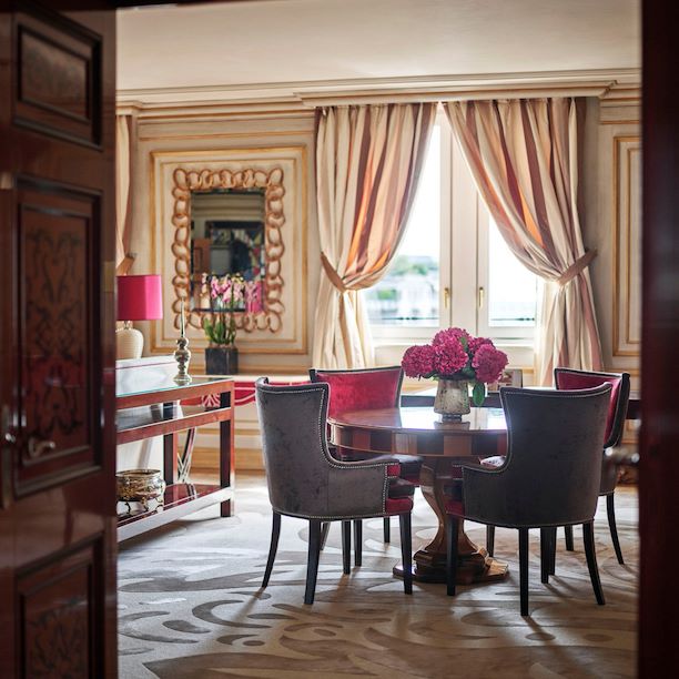 Executive Suite Living Room furnished with a wooden table, four red velvet chairs and a bouquet of pink flowers