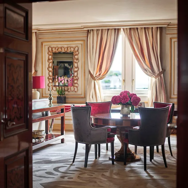 Executive Suite Living Room furnished with a wooden table, four red velvet chairs and a bouquet of pink flowers