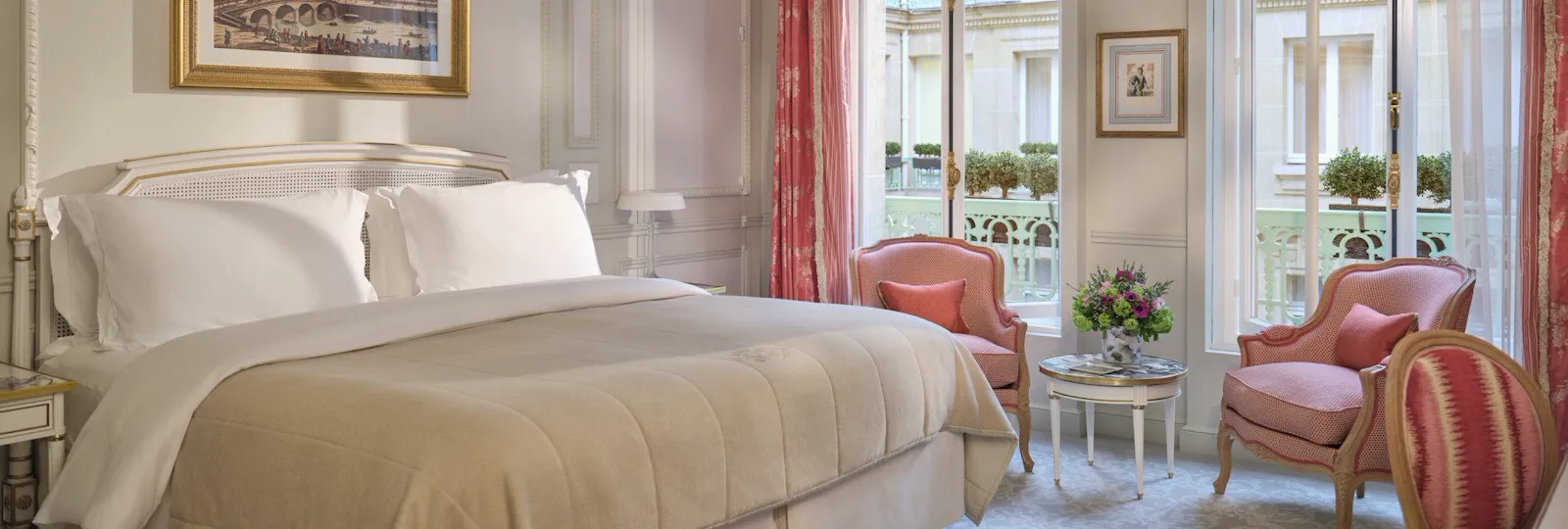 Large view of a Deluxe room with the bed, three chairs, the paintings and high windows, at Le Meurice, Paris