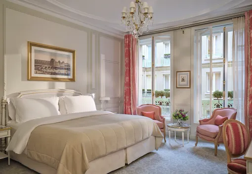 Large view of a Deluxe room with the bed, three chairs, the paintings and high windows, at Le Meurice, Paris