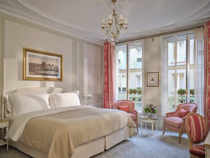 Large view of a Deluxe room with the bed, three chairs, the paintings and high windows, at Le Meurice, Paris