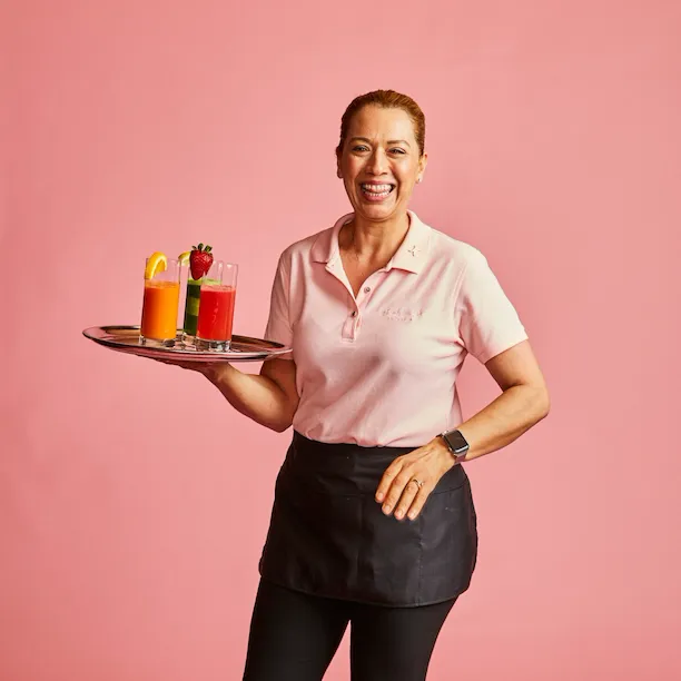 Woman holding three drinks against a pink background