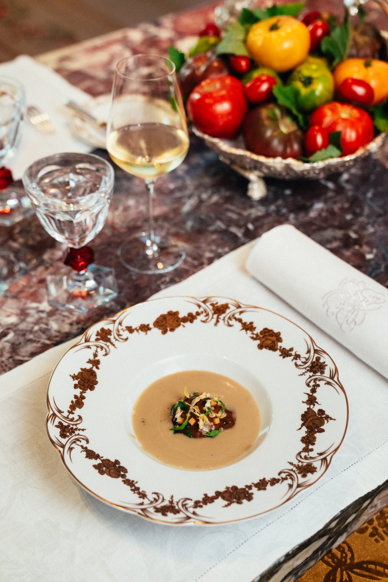 Empty plate with food, wine glass, fruit bowl, and napkin on a marble table.