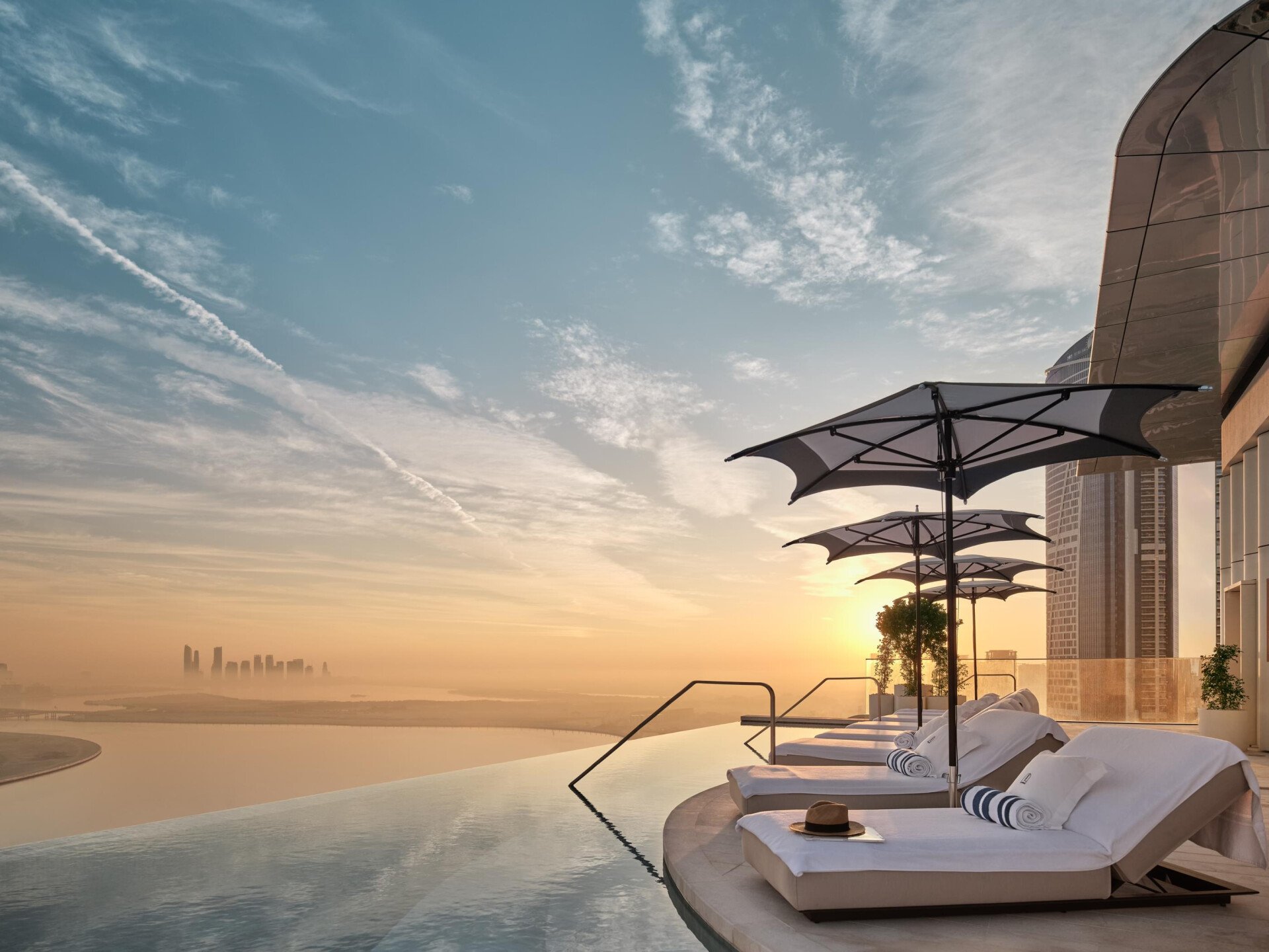 Sunloungers by The Lana's rooftop infinity pool at sunrise with view of Dubai