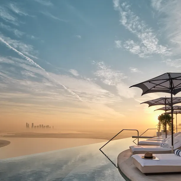Sunloungers by The Lana's rooftop infinity pool at sunrise with view of Dubai