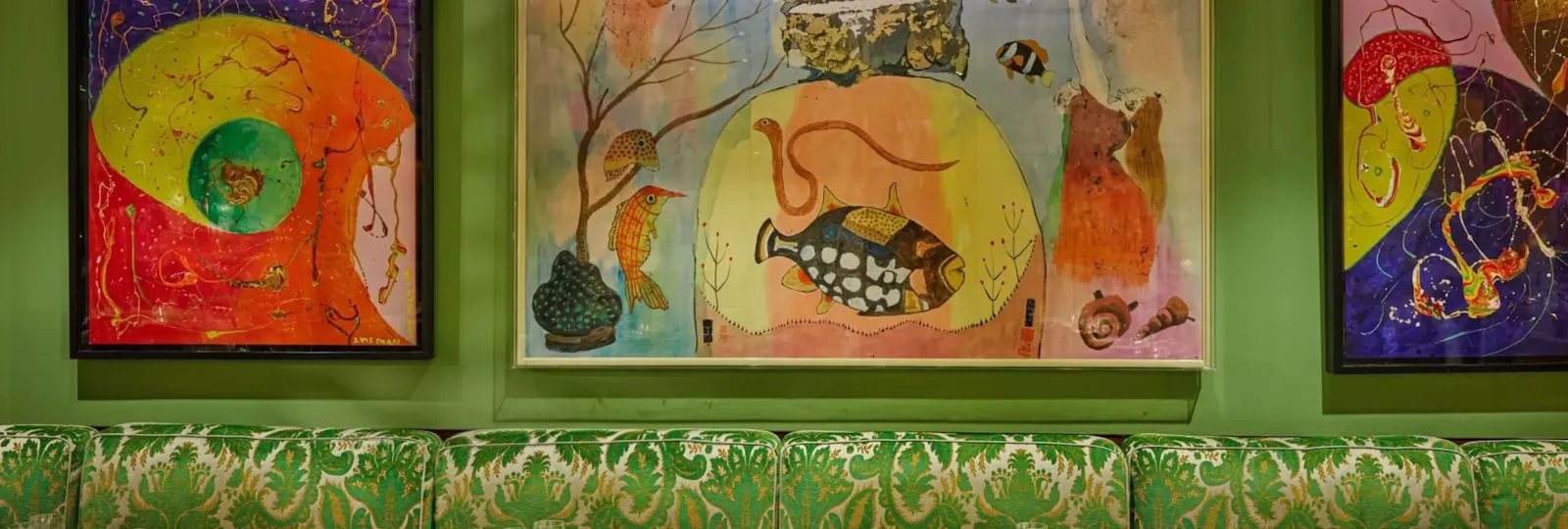 Interior dining space at China Tang at The Dorchester, showcasing colourful contemporary artworks displayed against green walls, patterned upholstered banquette seating and tables set with fine tableware and glassware.