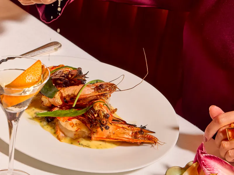 Guest squeezing fresh lime over a prawn dish at The Grill at The Dorchester, with a Martini, side salad and Ginori tableware visible.