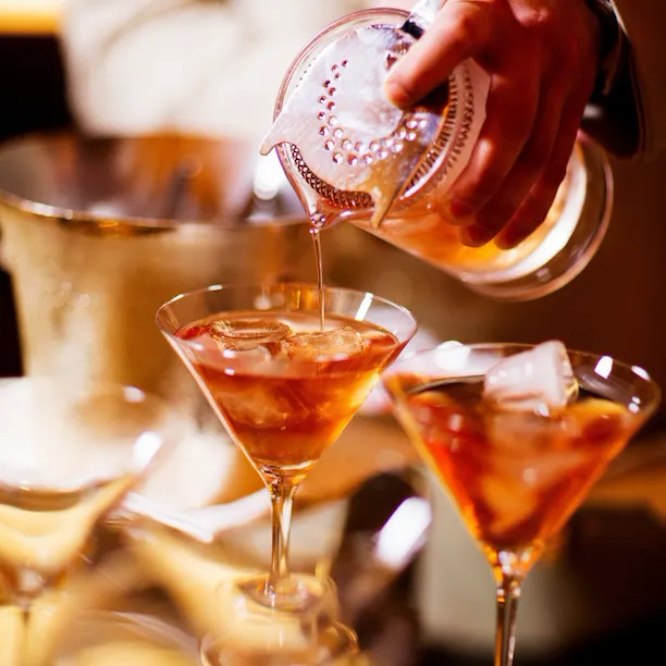 Barman pouring cocktails into Martini glasses at La Libreria at Hotel Eden, Rome