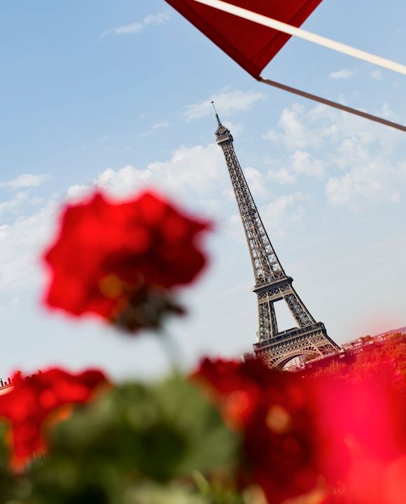 View of Eiffel Tower from balcony with red flowers in foreground at Hôtel Plaza Athénée, Paris
