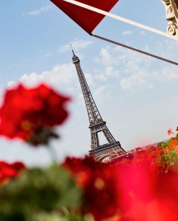 View of Eiffel Tower from balcony with red flowers in foreground at Hôtel Plaza Athénée, Paris