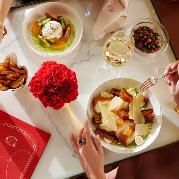 Femmes déjeunant à La Galerie, vue de leurs mains choisissant des frites et mangeant une salade César, salade McCarthy et vin blanc sur la table, à l'Hôtel Plaza Athénée, Paris