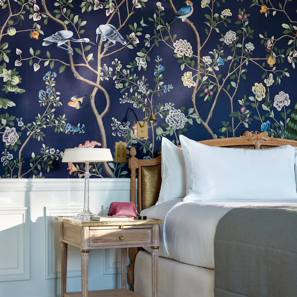 Portrait de la table de chevet dans une chambre exécutive, avec une pochette et un livre placé sur la table. Le lit met en valeur le mur peint à la main bleu foncé. Au Meurice, Paris.