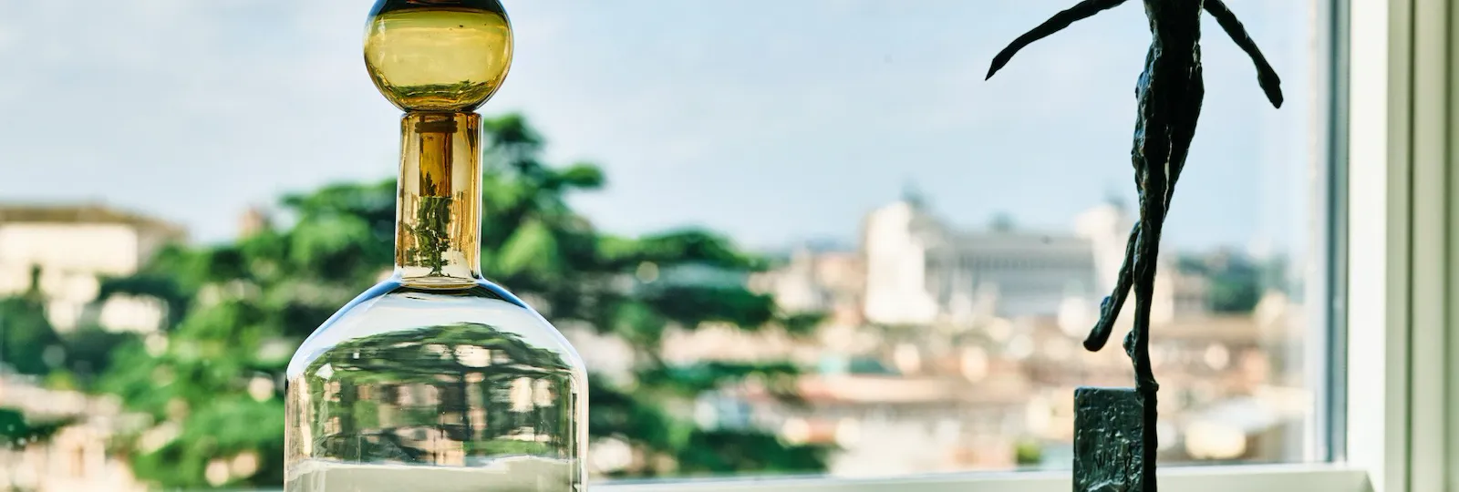 Scultura di figura umana co le braccia spalancate e vaso di vetro su un mobile nel salotto della Suite Penthouse Bellavista a Hotel Eden Roma