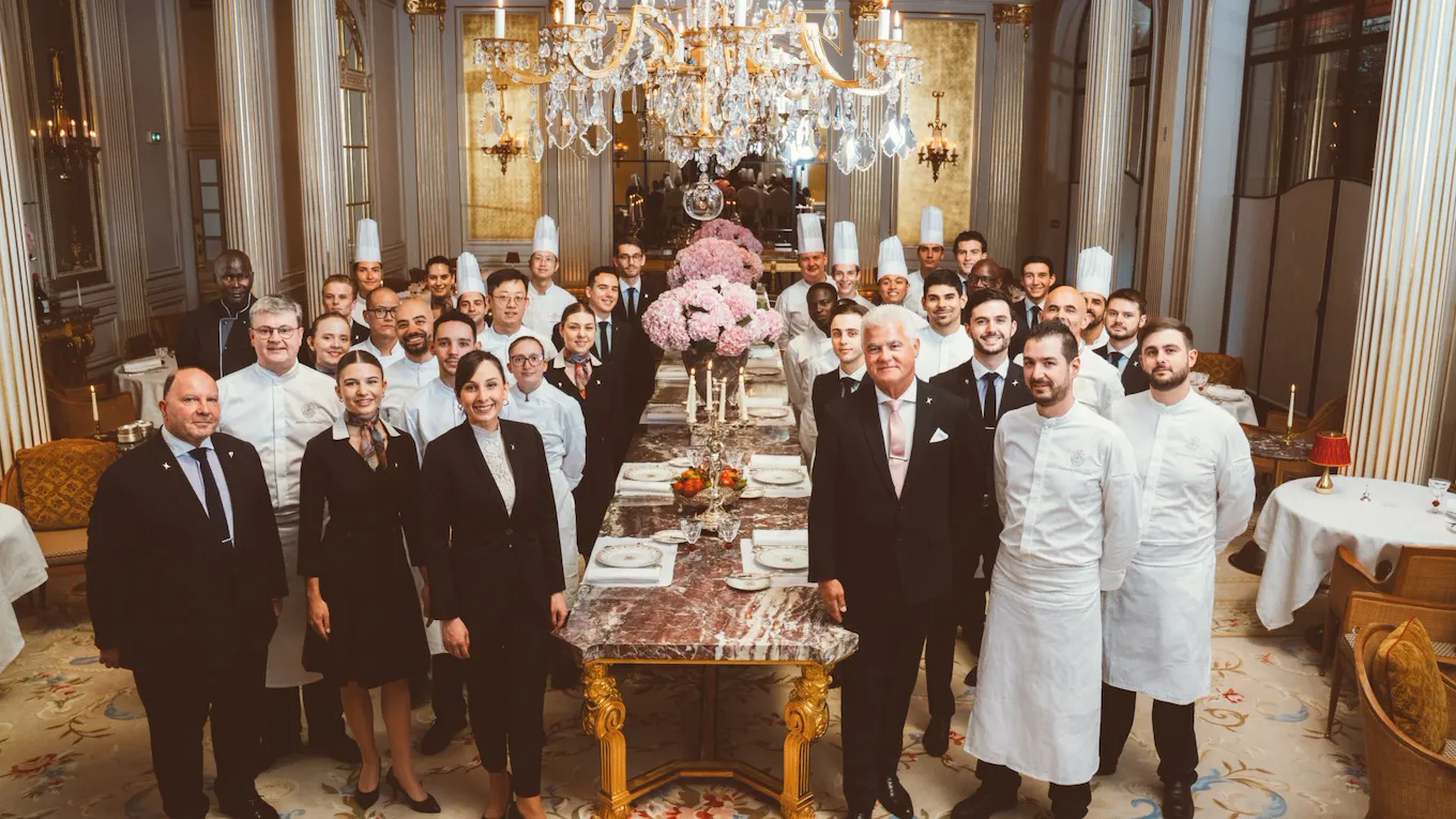 Group of people in formal attire and chef uniforms in a decorated dining room with a long table.