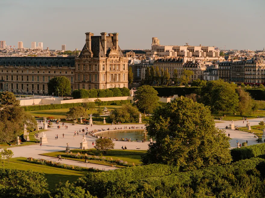 Aerial view of the Tuileries gardens with a smooth yellow light, at sunset. A pond with a fountain and chairs around it is at the center of the picture, at the Tuileries gardens, Paris