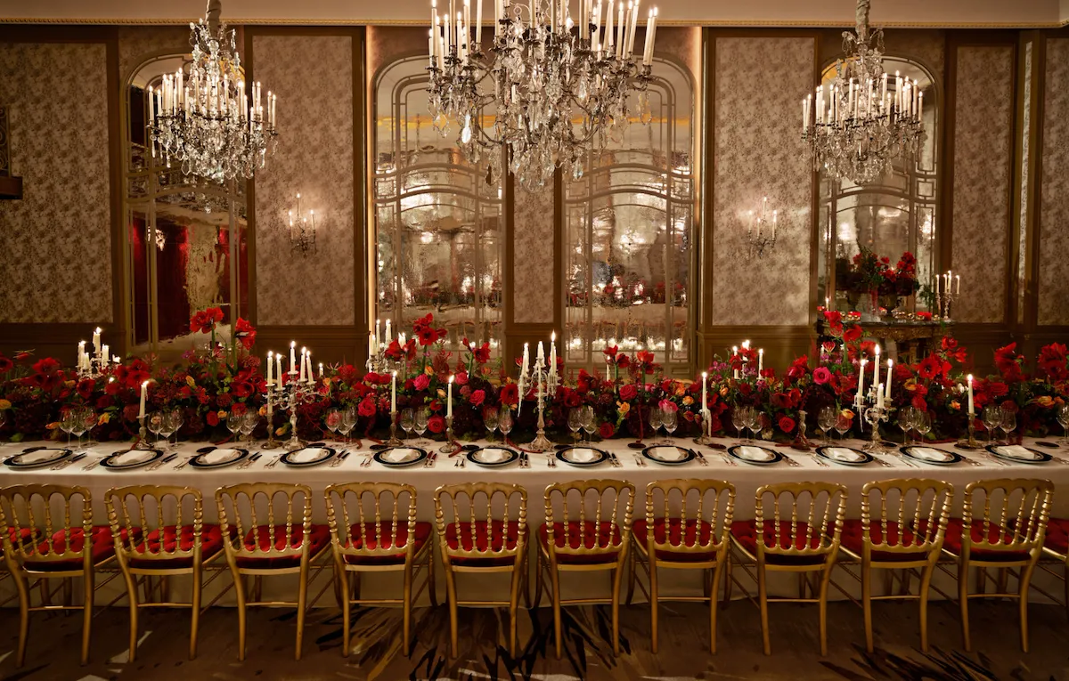 Dinner set up with a long table and red flowers captured in Le Salon Haute Couture, at Hôtel Plaza Athénée, Paris - Dorchester Collection.