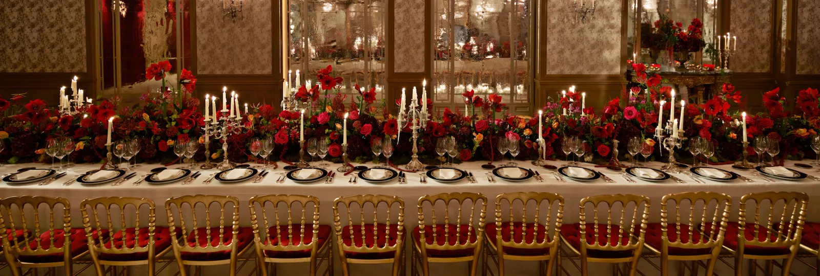 Dinner set up with a long table and red flowers captured in Le Salon Haute Couture, at Hôtel Plaza Athénée, Paris - Dorchester Collection.