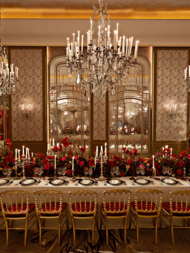 Dinner set up with a long table and red flowers captured in Le Salon Haute Couture, at Hôtel Plaza Athénée, Paris - Dorchester Collection.