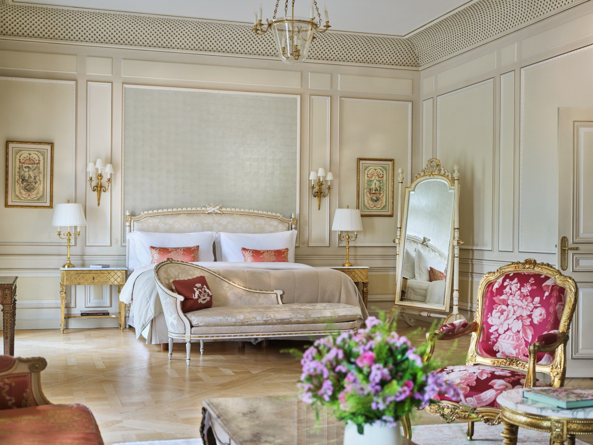 Grande vue d'une suite Versailles avec au premier plan un bouquet de fleurs et des chaises, et derrière un canapé près du lit, au Meurice, Paris