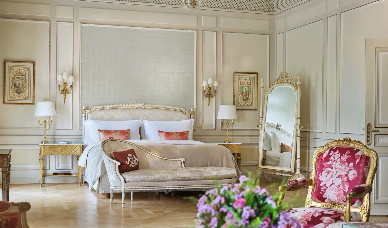 Grande vue d'une suite Versailles avec au premier plan un bouquet de fleurs et des chaises, et derrière un canapé près du lit, au Meurice, Paris