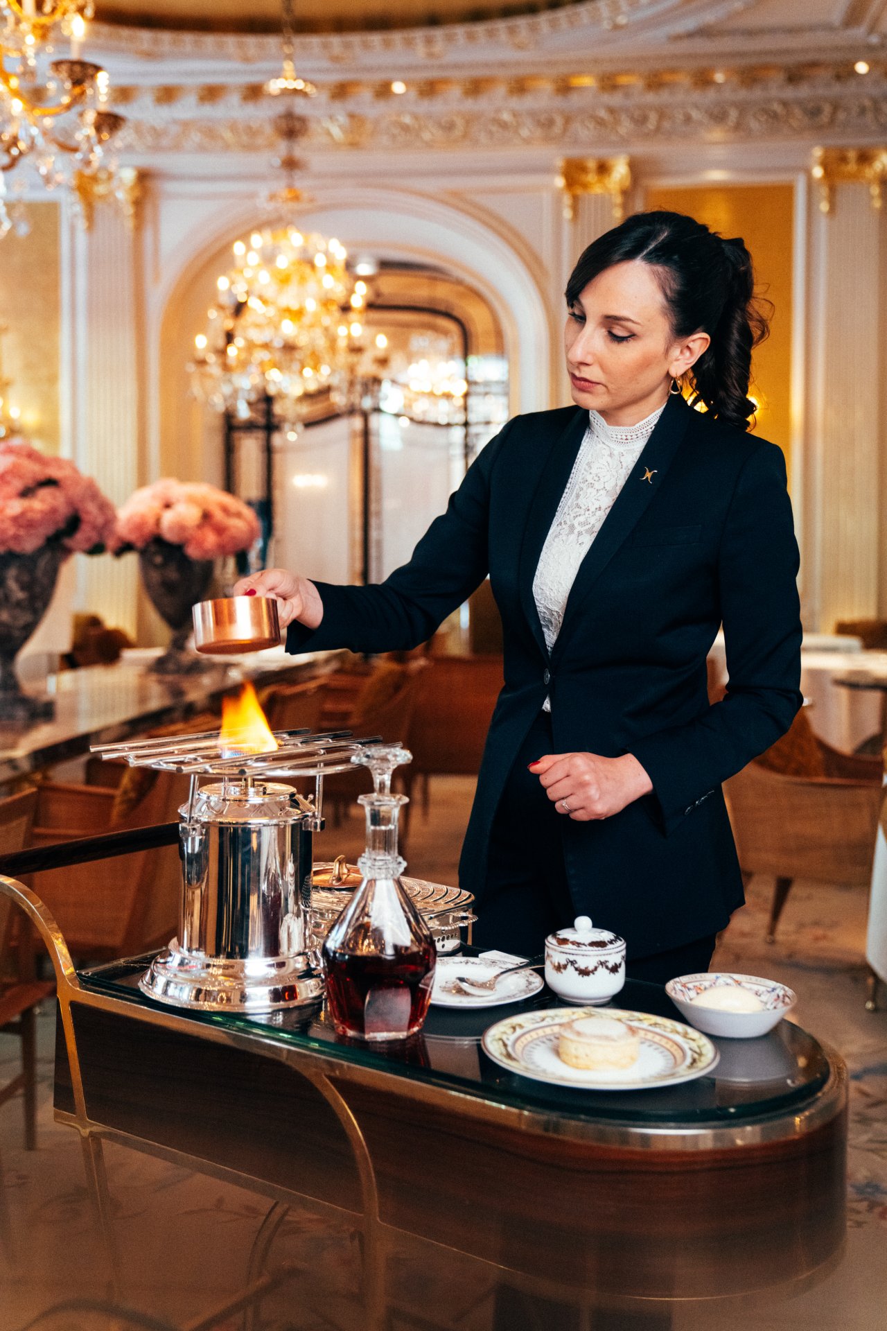 Person in formal attire conducts a flaming demonstration at a luxurious indoor setting.