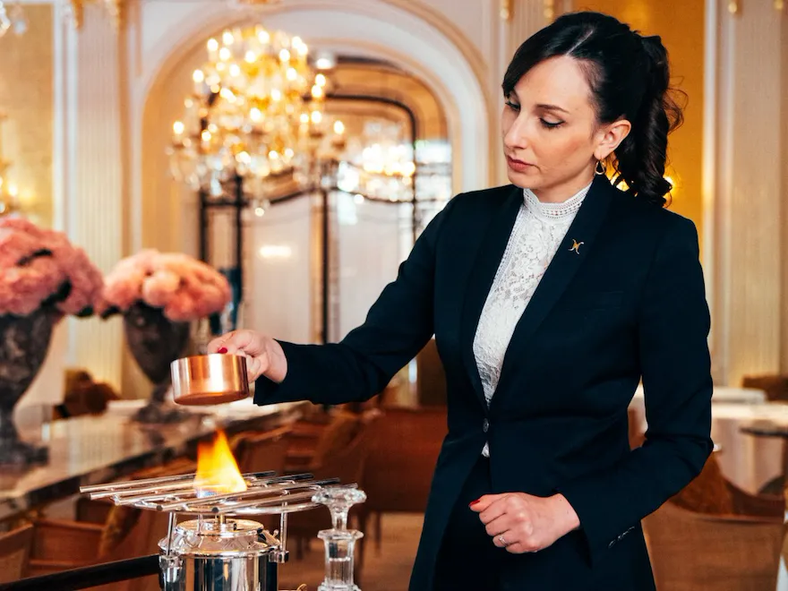 Person in formal attire conducts a flaming demonstration at a luxurious indoor setting.