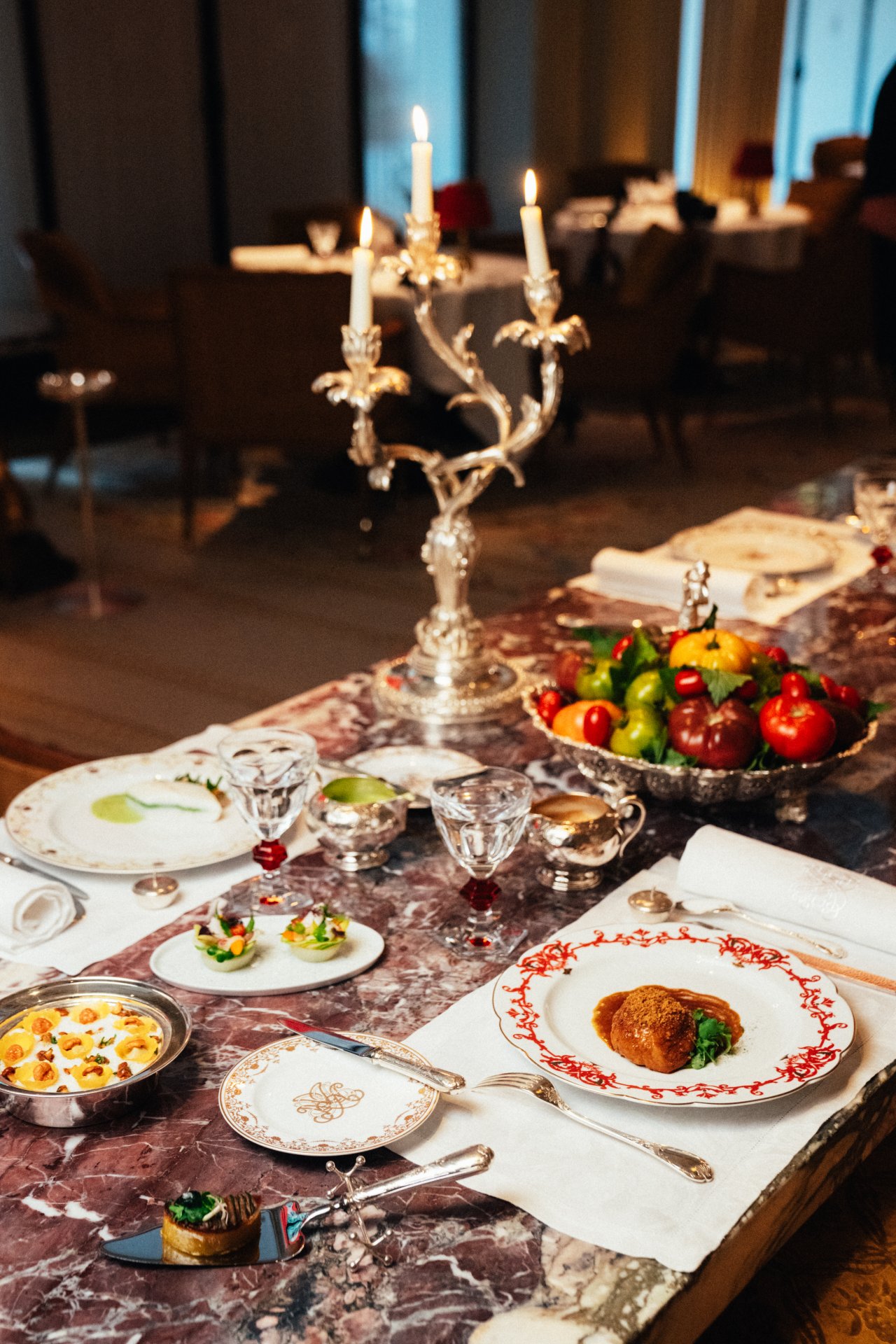 A decorated table with a candelabrum, plates of food, fruits, and glasses in a formal dining setting.