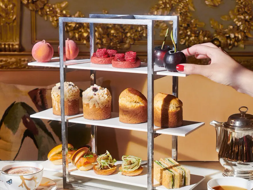 Au premier plan, une assiette et deux tasses de café et au centre, un étalage de gâteaux avec brioche, pâtisseries et fruits trompe l'oeil de Cédric Grolet qui apporte beaucoup de couleur à la photo, au Meurice, Paris