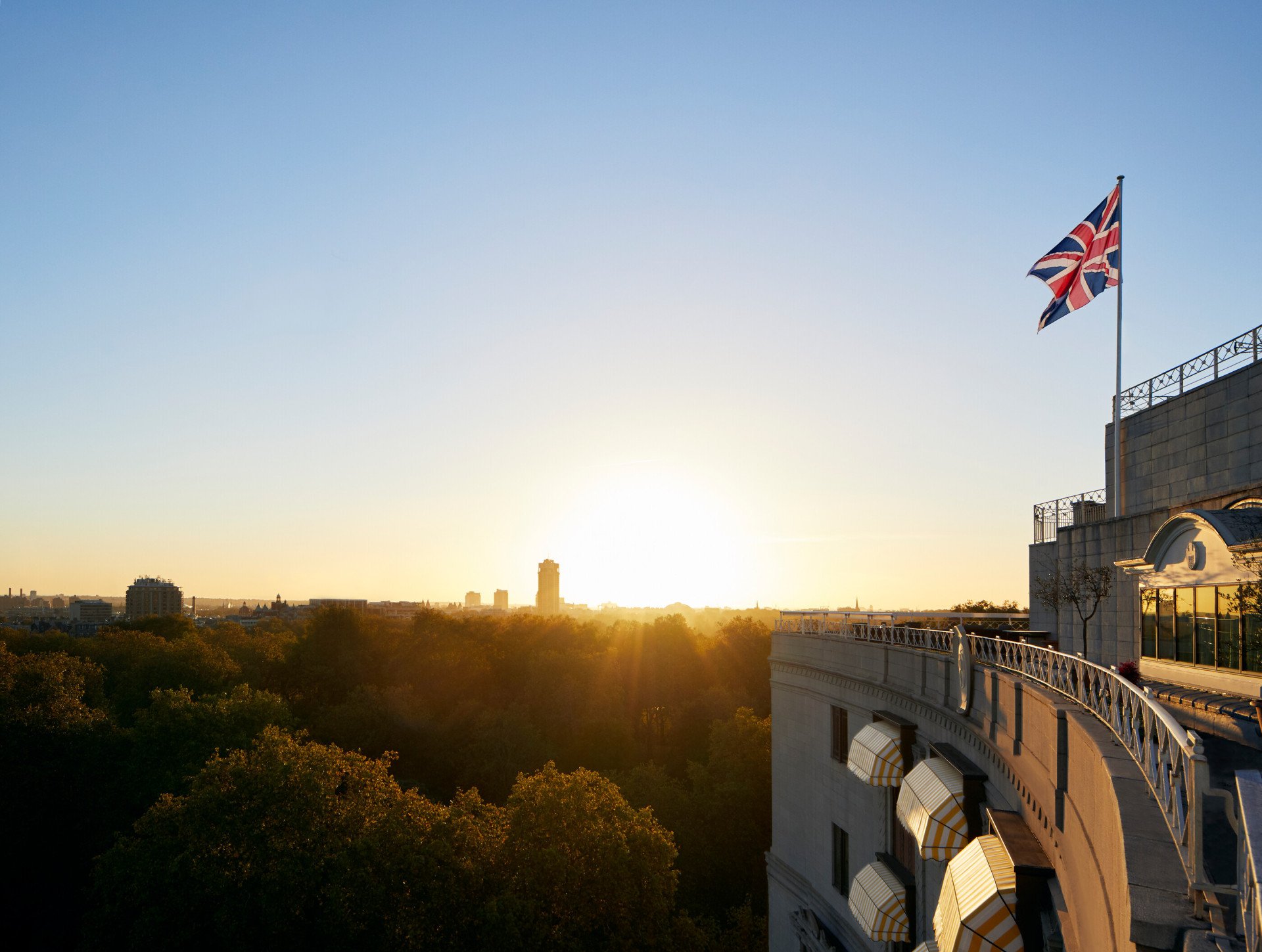 The Union Jack flag flying from the top of The Dorchester overlooking Hyde Park at sunset, London